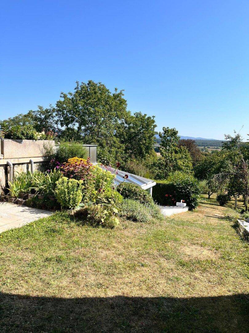 Sonnige Gartenanlage mit vielfältiger Bepflanzung und weitem Blick über die grüne Landschaft.