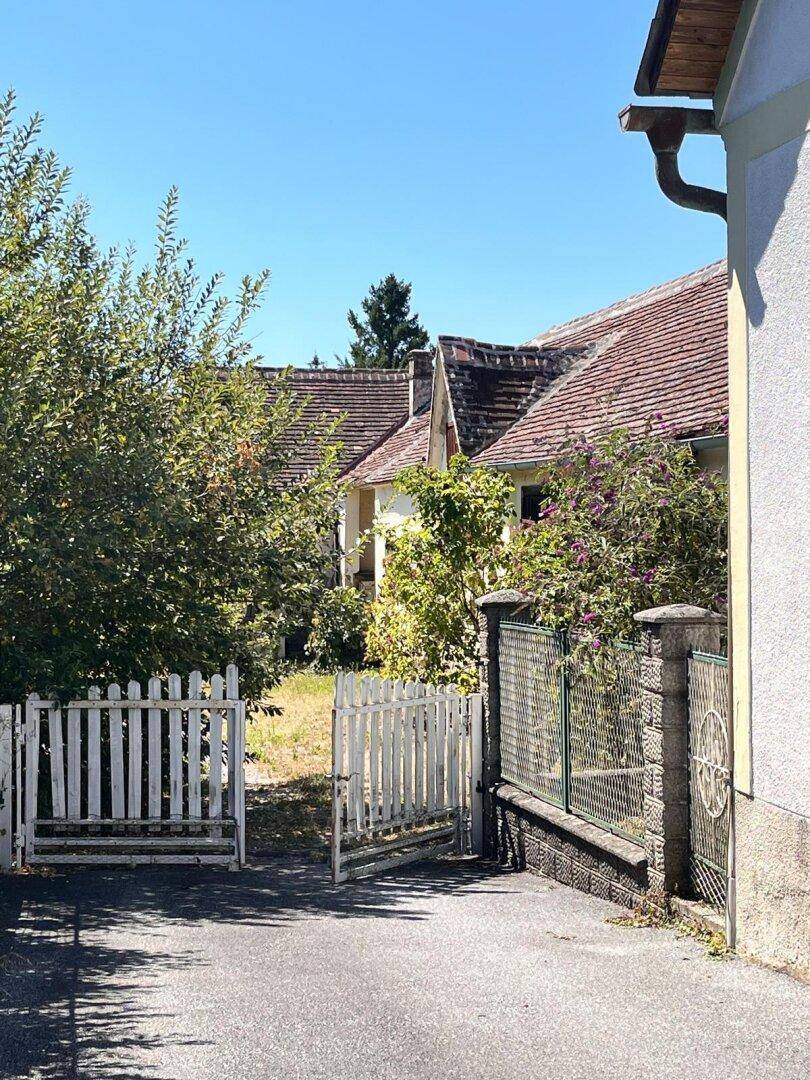 Weißes Holztor und Zaun, der zu einem weiteren, grünen Bereich des Grundstücks führt.