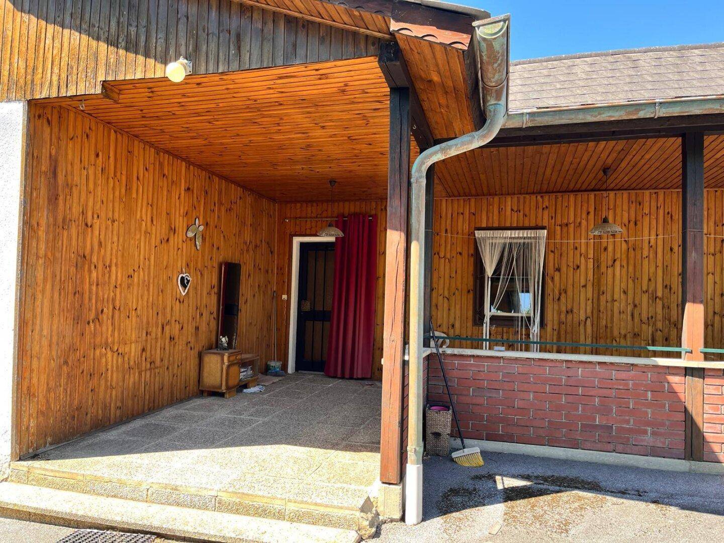 Überdachter Eingangsbereich des Hauses mit rustikaler Holzverkleidung und Steinfliesenboden.