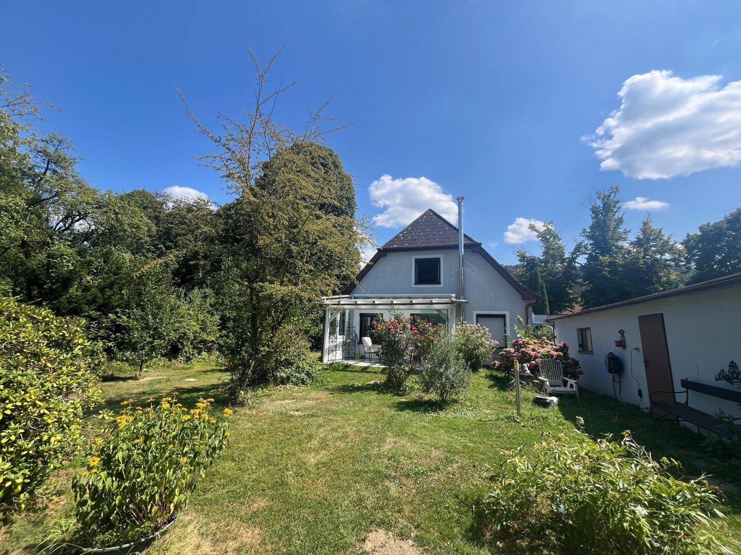 Rückansicht des Hauses mit überdachter Terrasse und weitläufigem, grünem Gartenbereich.