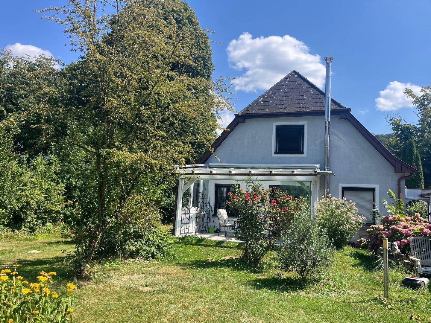 Rückansicht des Hauses mit überdachter Terrasse und weitläufigem, grünem Gartenbereich.