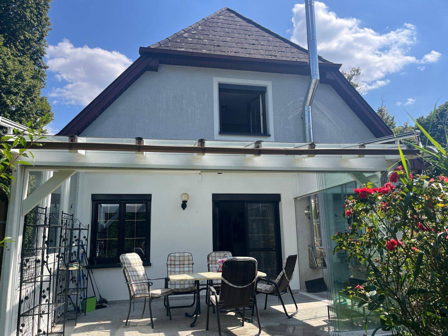 Überdachte Terrasse mit Gartentisch und Stühlen, ideal für Mahlzeiten im Freien.