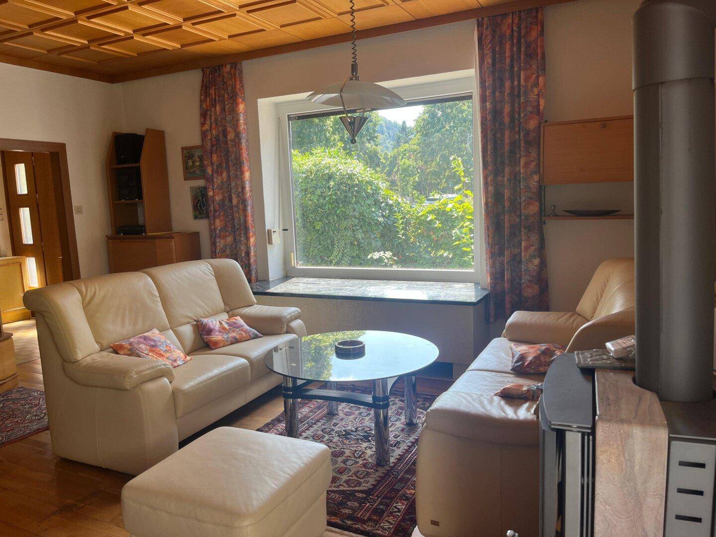 Helles Wohnzimmer mit beigen Ledersofas, Holzkassettendecke und Blick ins Grüne.