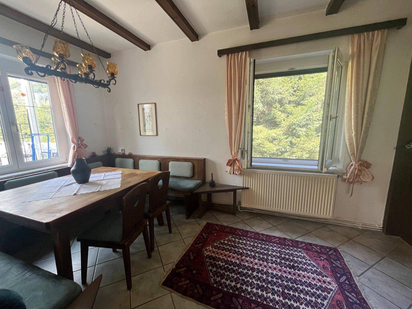 Essbereich mit Holztisch, Sitzbank und Blick in den Garten, ergänzt durch sichtbare Deckenbalken.