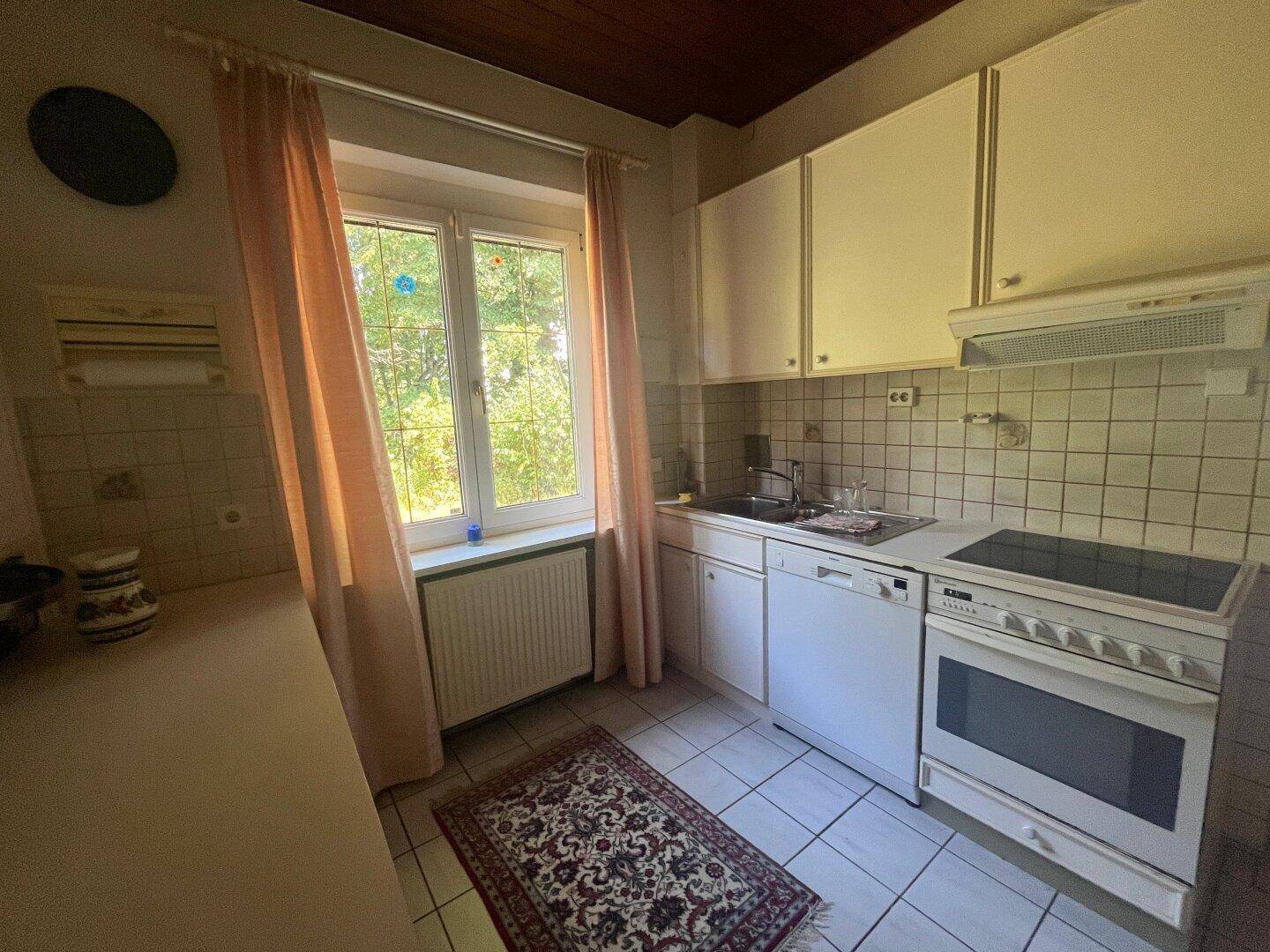 Funktionale Küche mit weißen Schränken, Fliesenboden und Fenster mit Blick ins Grüne.