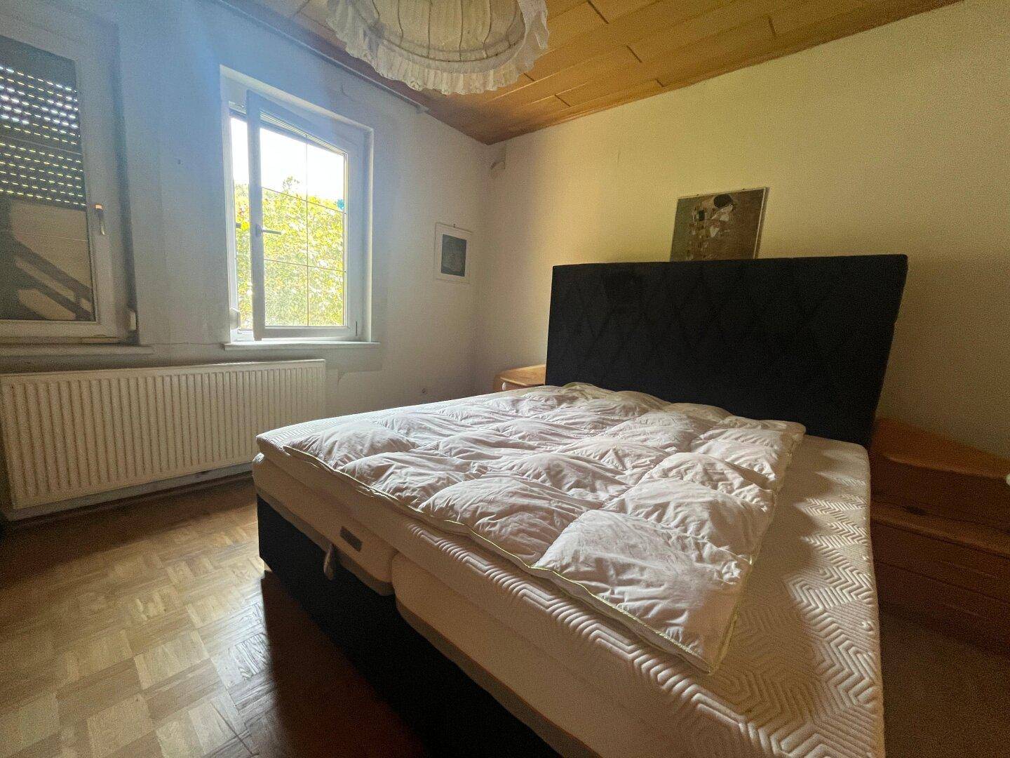 Schlafzimmer mit Doppelbett, Holzkassettendecke und Fenster mit Blick ins Grüne.