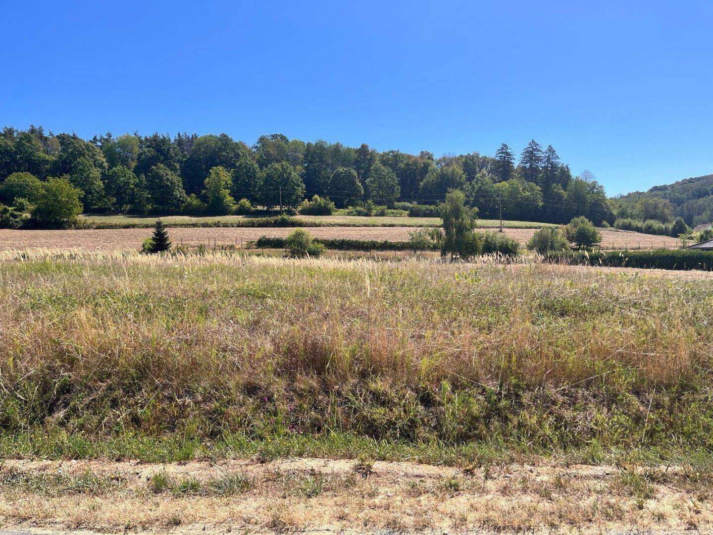 Offene Landschaft mit Feldern, bewaldeten Hügeln und einem weiten blauen Himmel.