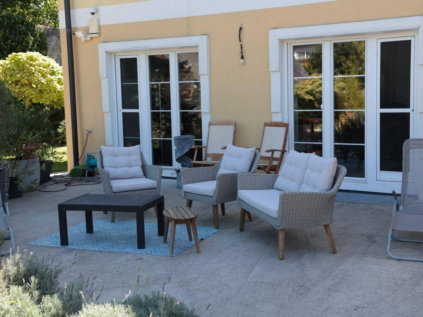 Gemütliche Terrasse mit Korbsesseln und einem kleinen Tisch, direkt vor großen Glastüren des Hauses.