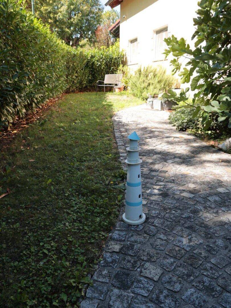 Gepflasterter Weg führt entlang eines Rasens und einer Hecke, mit einem dekorativen Leuchtturm.