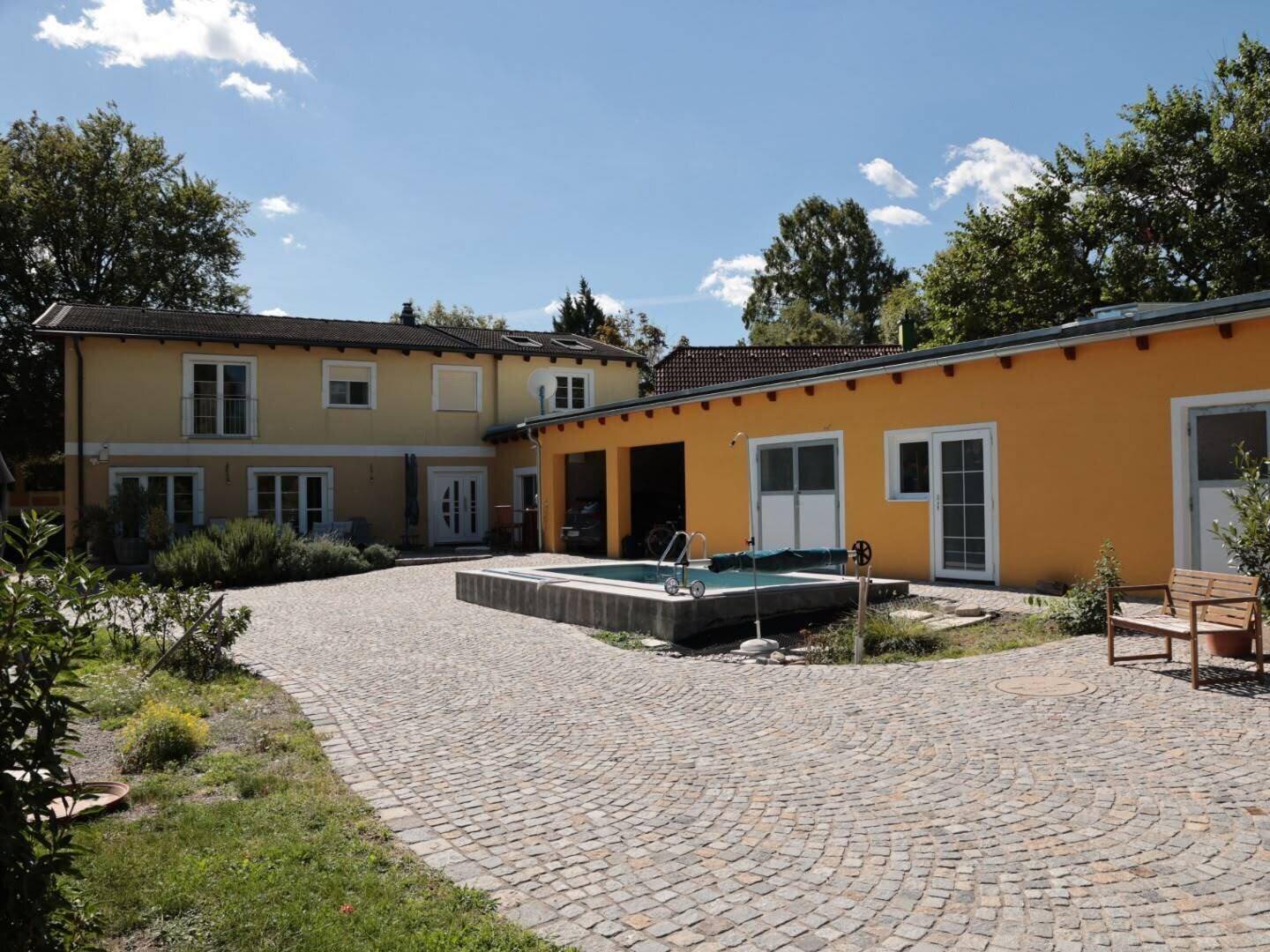 Weitläufiger Außenbereich des Anwesens mit gelbem Haupthaus, Pool und einem weiteren Gebäude, verbunden durch einen gepflasterten Hof.