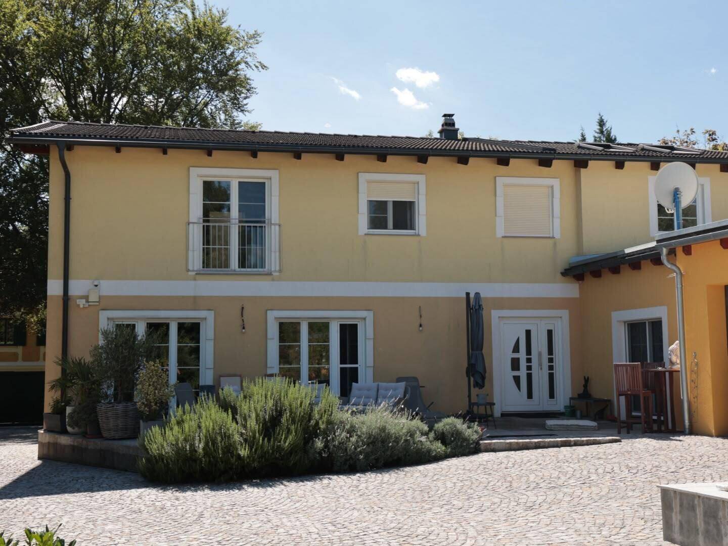 Gelbe Hausfassade mit weißen Akzenten, Fenstern, einem kleinen Balkon und einer möblierten Terrasse.