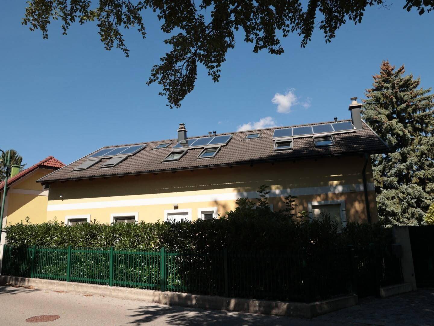 Seitenansicht eines gelben Hauses mit Satteldach, vielen Dachfenstern und Solarpaneelen auf dem Dach.