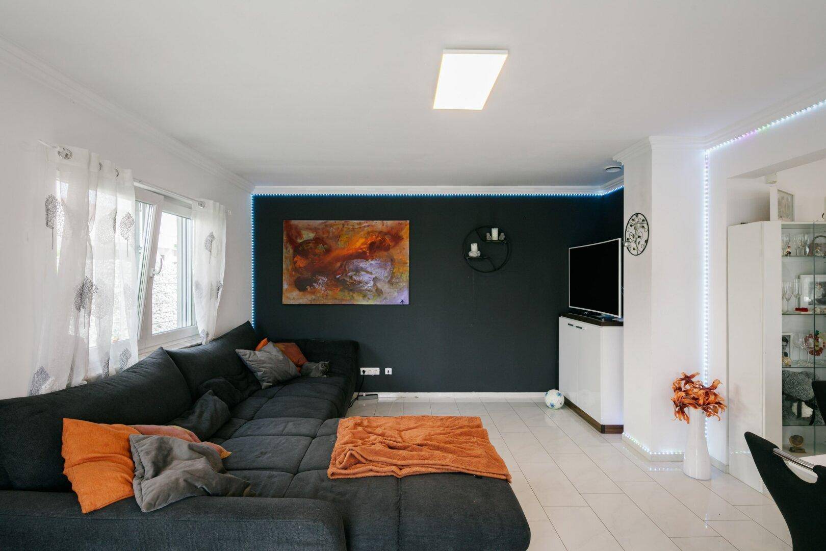 Gemütliches Wohnzimmer mit großem Ecksofa, dunkler Akzentwand und dekorativer LED-Beleuchtung.