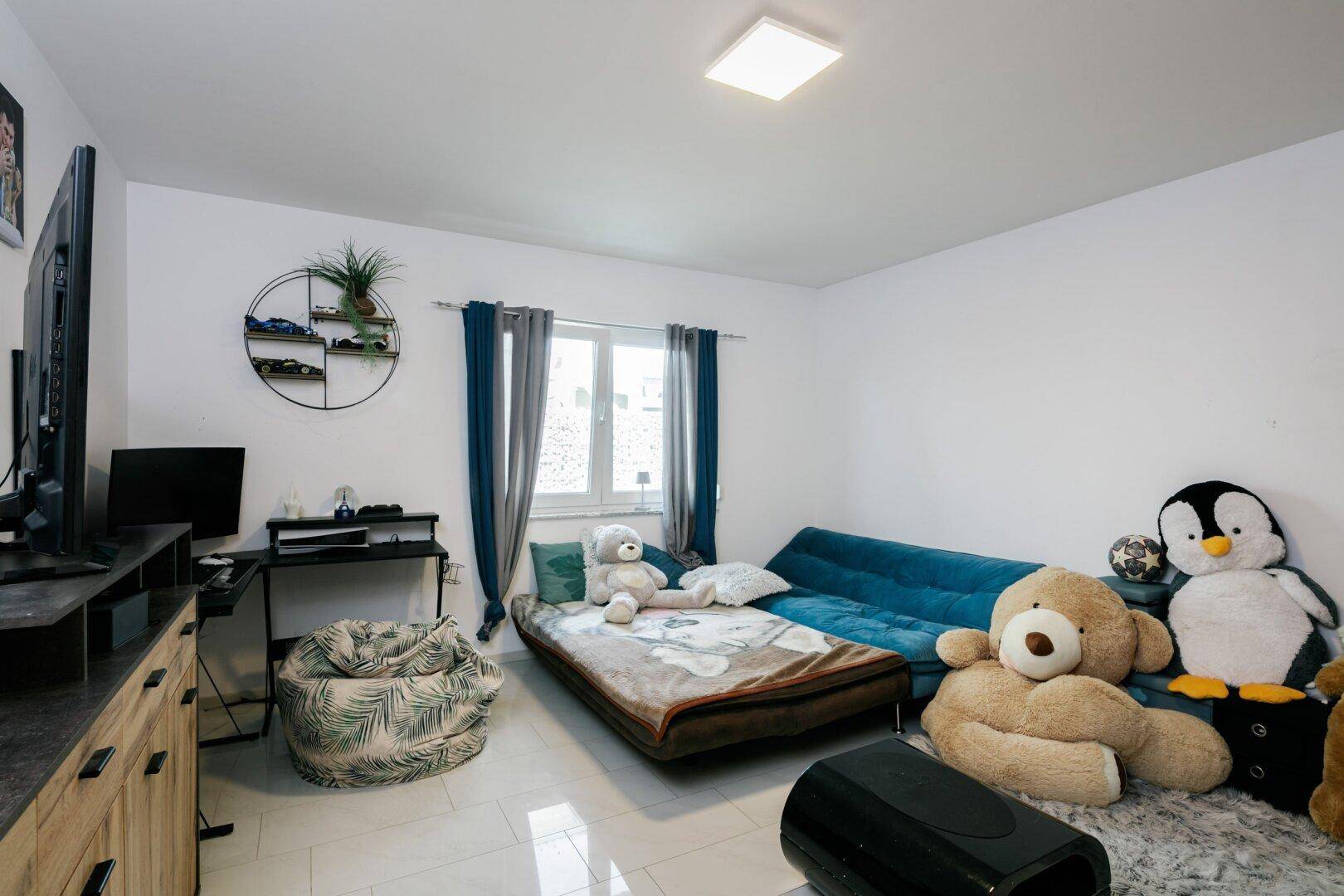 Kinderzimmer oder Gästezimmer mit Schlafsofa, vielen Plüschtieren und einem Schreibtischbereich.