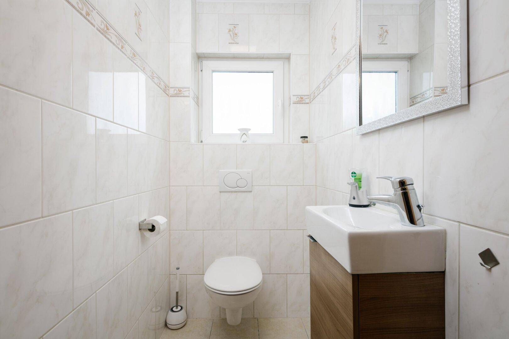 Kleines Gäste-WC mit wandhängendem WC, Waschbecken und Fenster für Tageslicht.