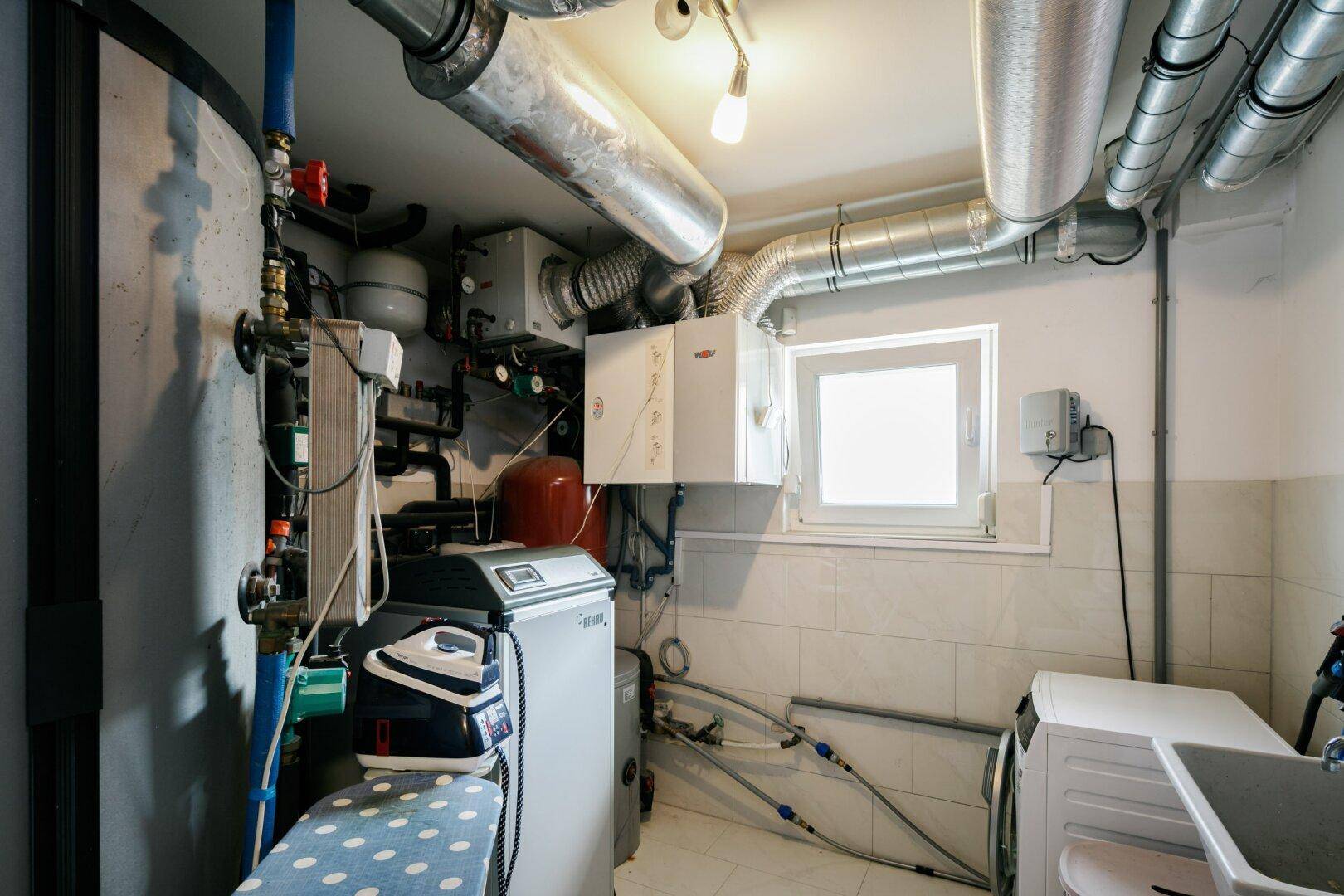 Hauswirtschaftsraum im Keller mit Heizungsanlage, Waschmaschine und Waschbecken.