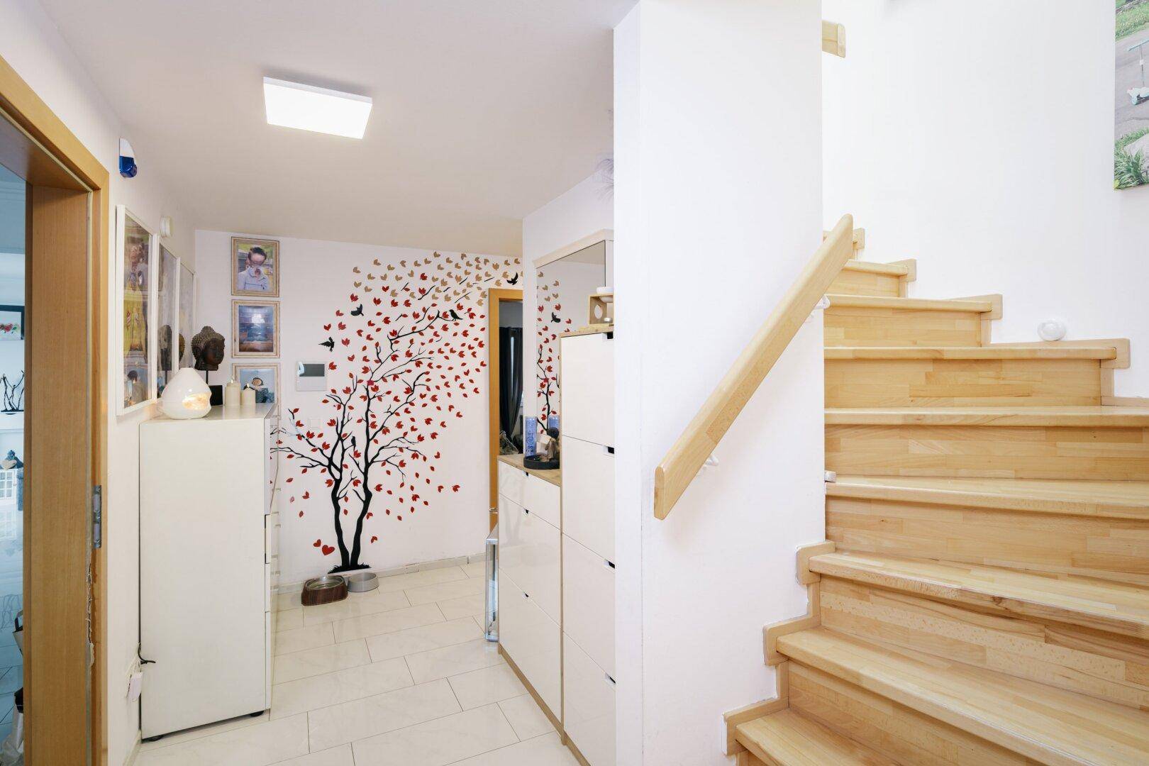 Heller Flur mit Holztreppe, Fliesenboden und dekorativer Wandgestaltung.
