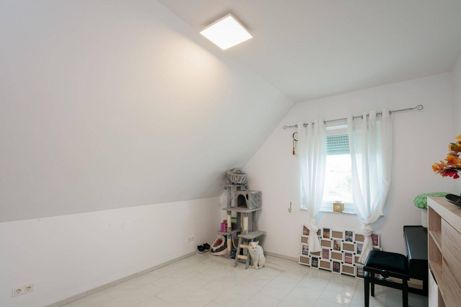 Dachgeschosszimmer mit schrägen Wänden, Fenster und hellem Fliesenboden.
