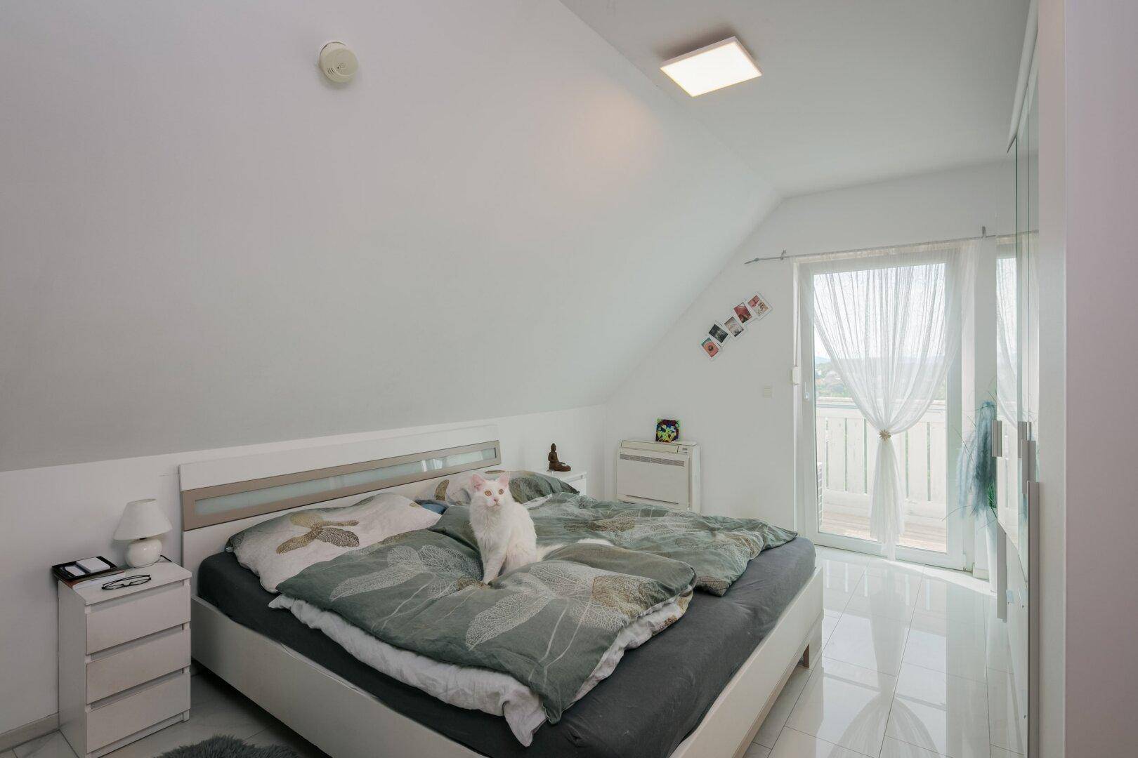 Schlafzimmer im Dachgeschoss mit Doppelbett, Kleiderschrank und Zugang zum Balkon.