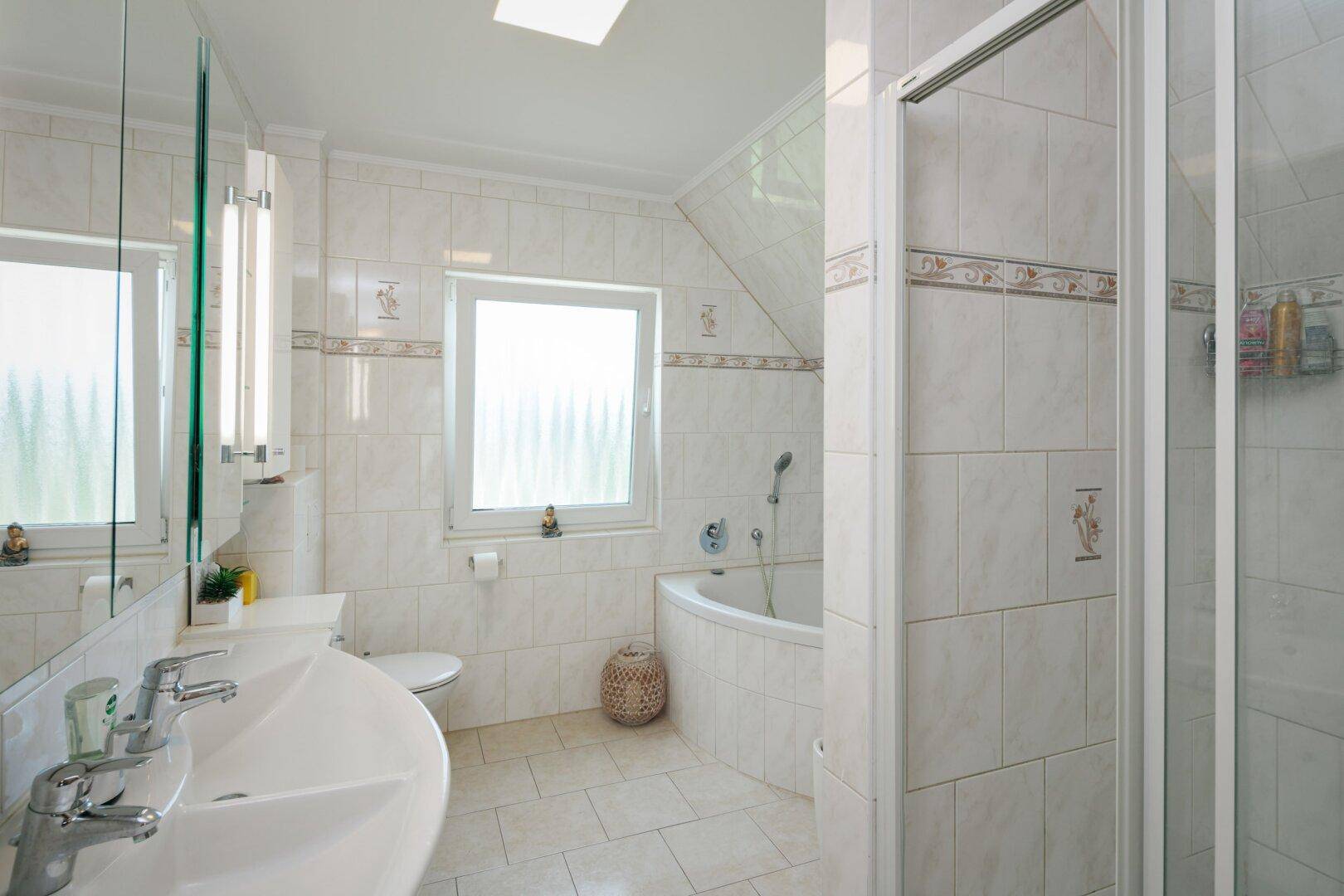 Helles Badezimmer mit Eckbadewanne, Dusche, Doppelwaschbecken und Fenster.