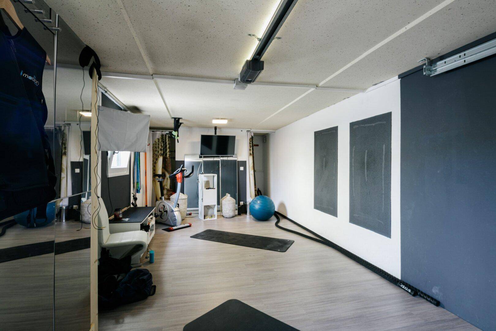Geräumiger Fitnessraum im Keller mit Sportgeräten, Spiegeln und dunklen Akzentwänden.