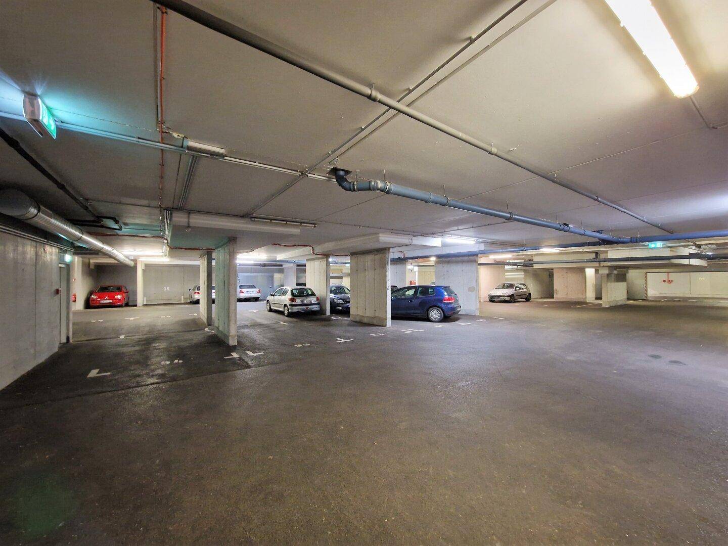 Weitläufige Tiefgarage mit markierten Stellplätzen, Säulen und verschiedenen geparkten Fahrzeugen.