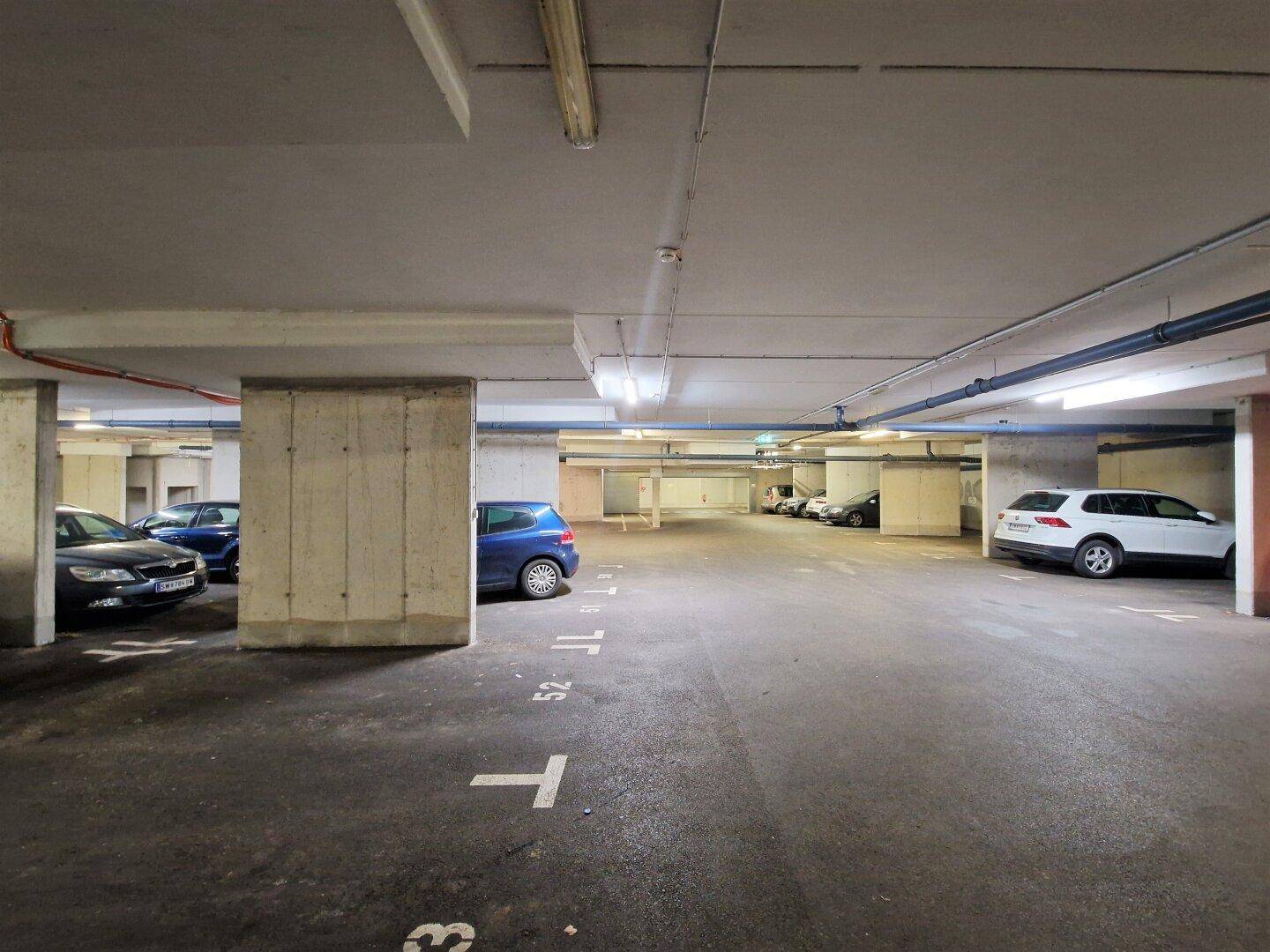 Übersichtliche Tiefgarage mit Betonpfeilern, nummerierten Stellplätzen und geparkten Autos.