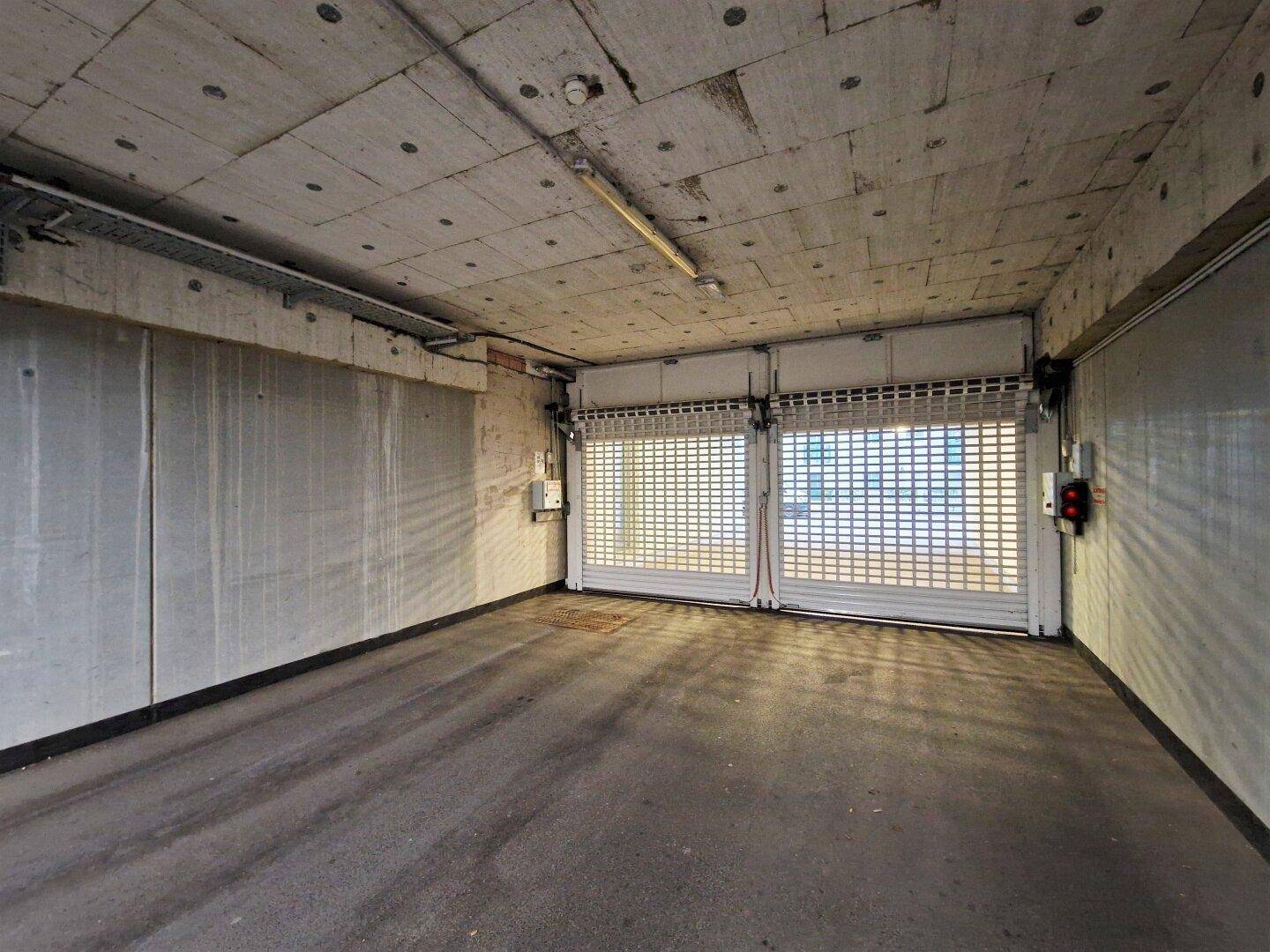 Leerer Garagenbereich mit zwei geschlossenen Rolltoren und Betonwänden, bereit für Fahrzeuge.