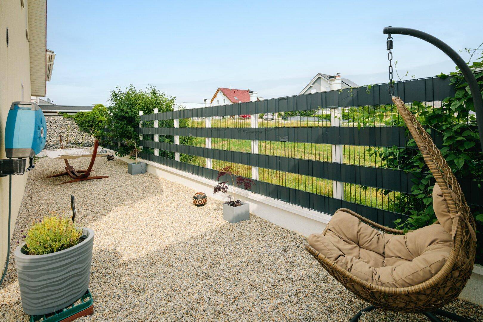 Kiesgarten mit Hängesessel und dekorativen Pflanzen, ideal zum Entspannen im Freien.