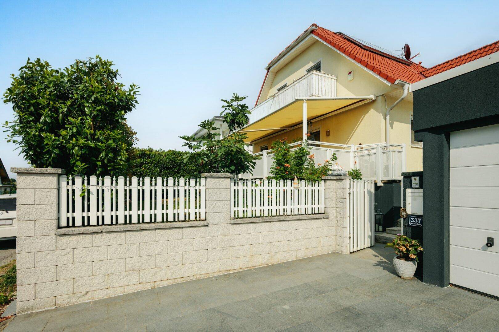 Einfamilienhaus mit weißem Lattenzaun, gepflasterter Einfahrt und Garage, gepflegtes Erscheinungsbild.