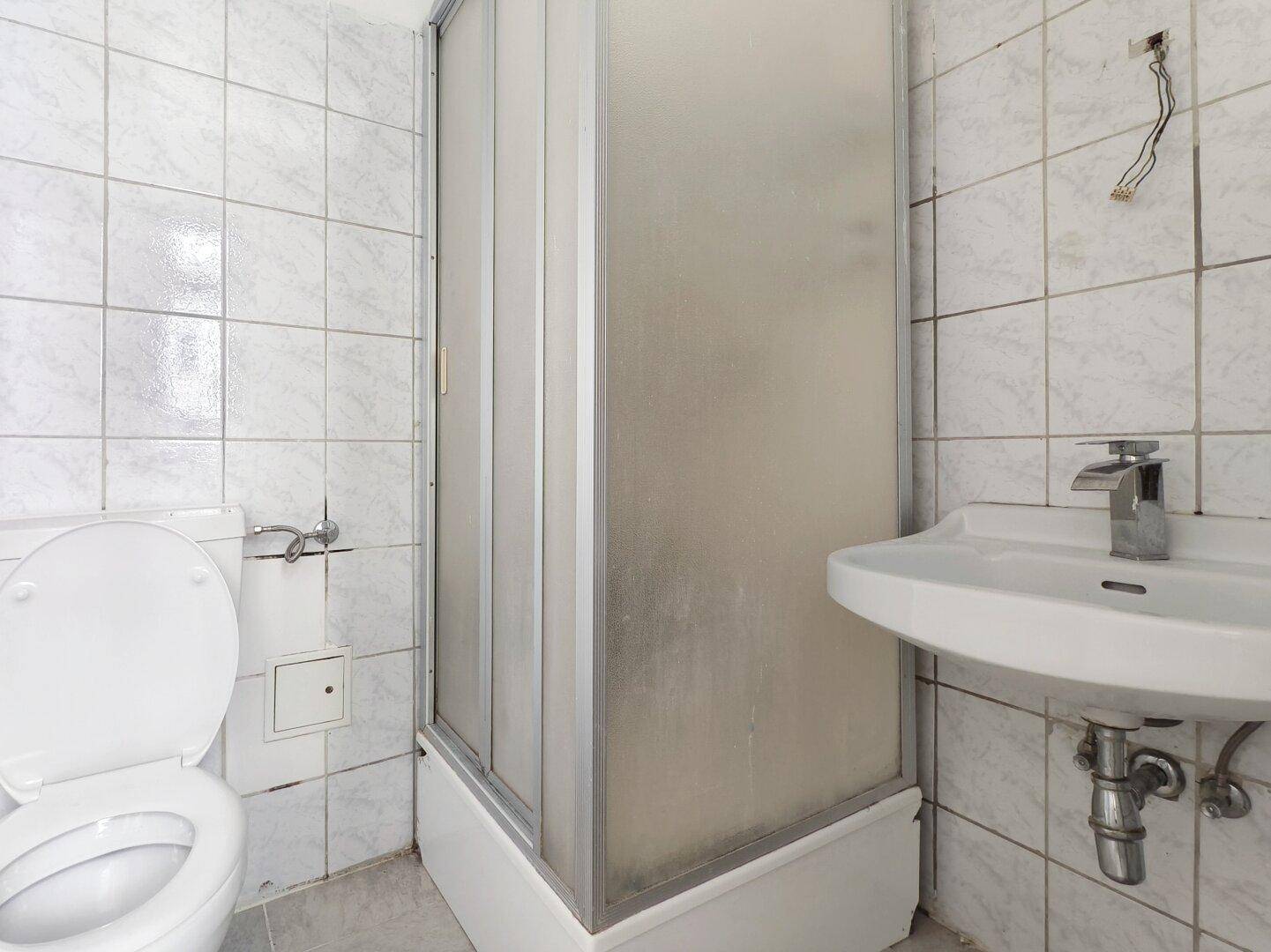 Kleines Badezimmer mit Toilette, Waschbecken und Duschkabine, einfach ausgestattet.