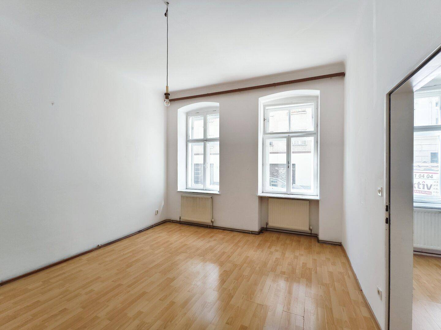 Leeres Zimmer mit Parkettboden und großen Fenstern, das viel Tageslicht hereinlässt.
