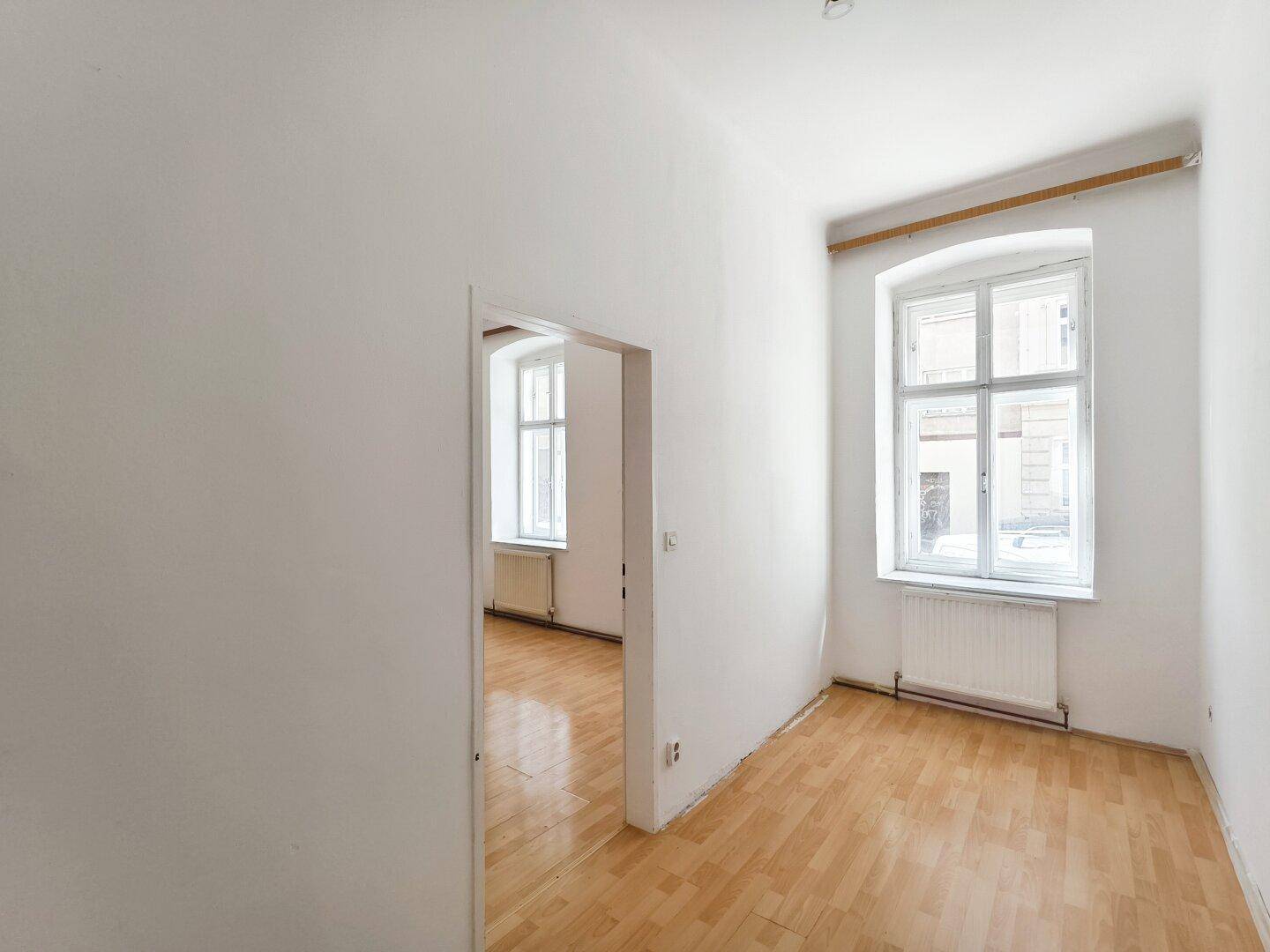 Zwei miteinander verbundene, helle Zimmer mit Parkettboden und hohen Decken.
