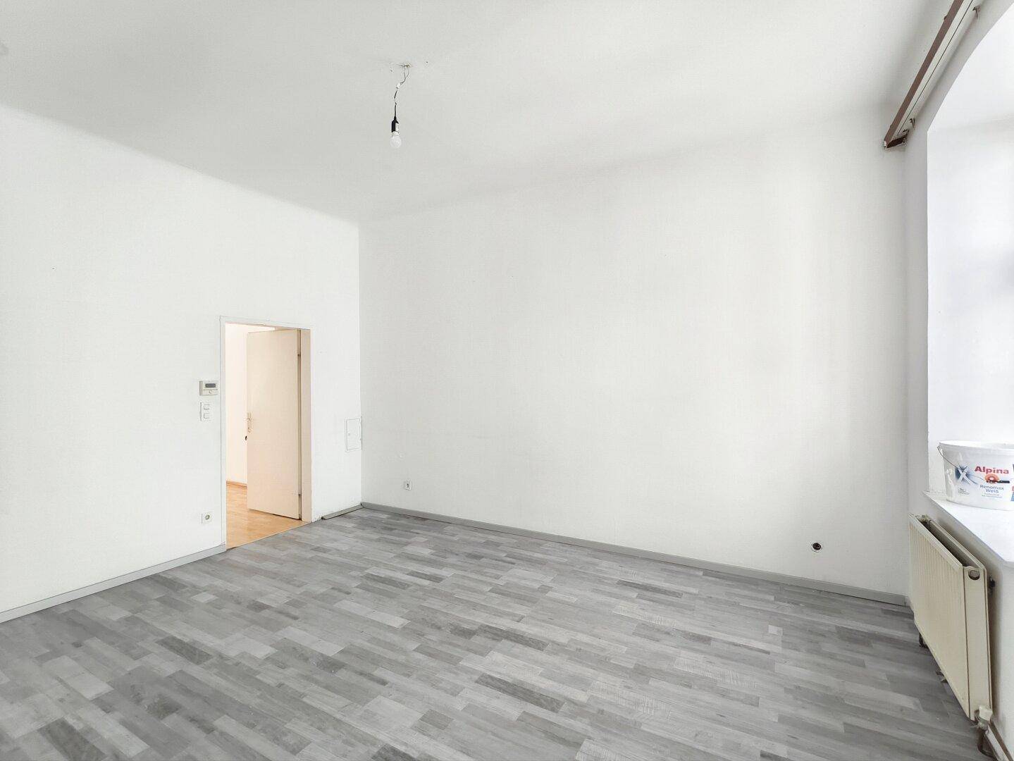 Helles, leeres Zimmer mit grauem Laminatboden und einem Fenster, ideal für individuelle Nutzung.