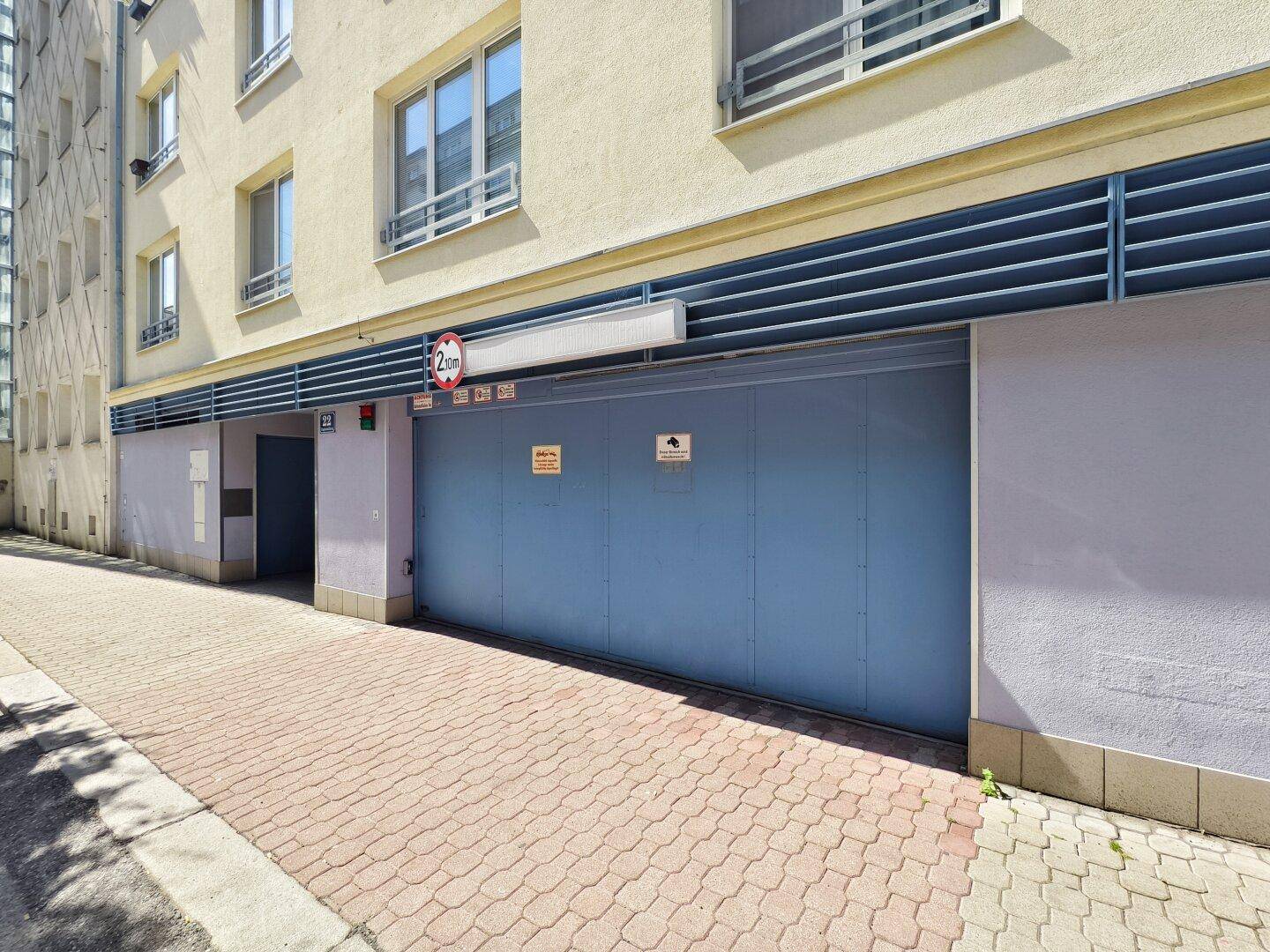 Schräge Ansicht der Tiefgarageneinfahrt mit gepflastertem Zugang und der Fassade des Wohngebäudes.