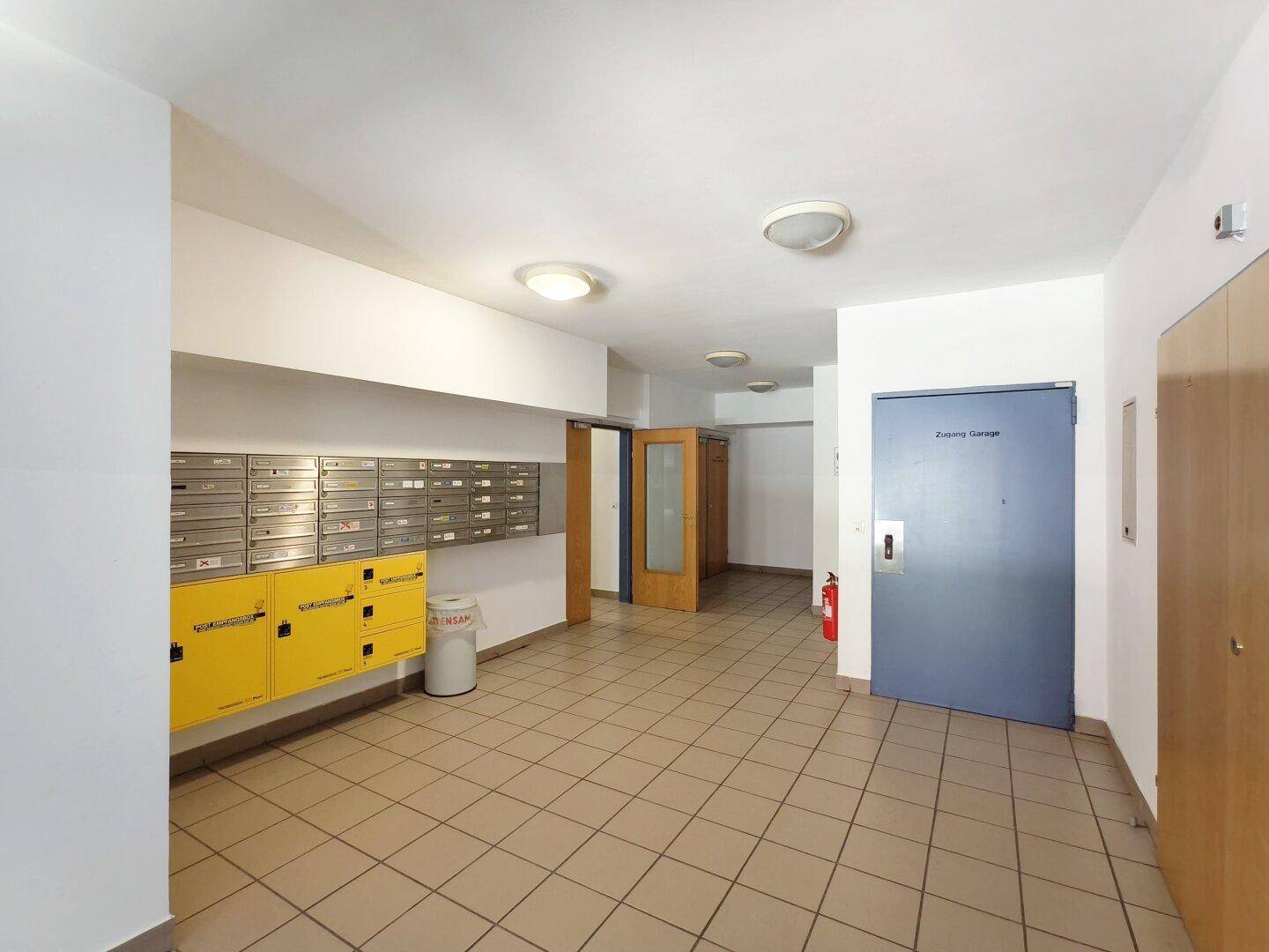 Heller Gemeinschaftsbereich mit Fliesenboden, Briefkästen und Zugangstür zur Tiefgarage.