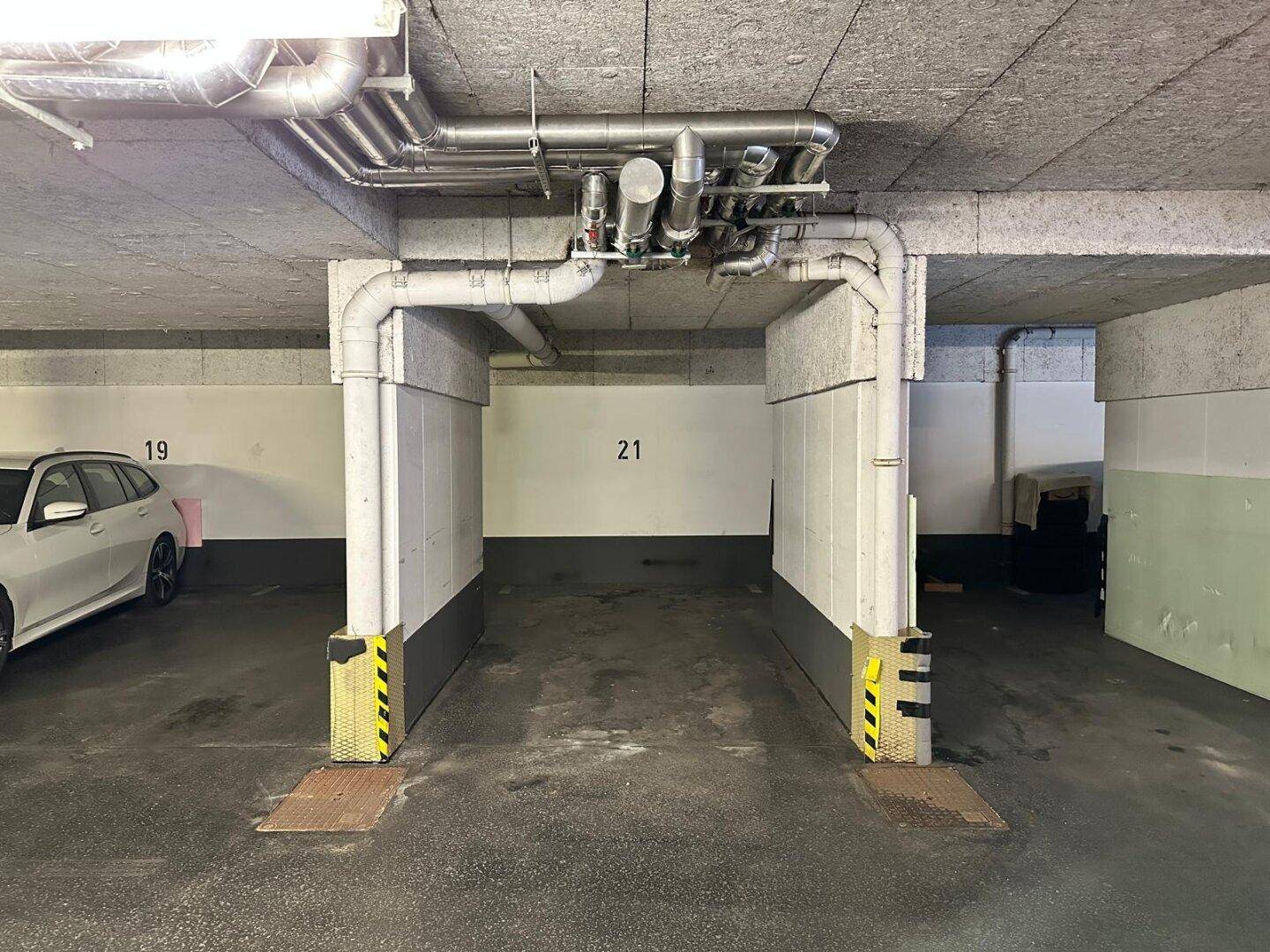 Tiefgarage mit Betonboden, sichtbaren Versorgungsleitungen an der Decke und nummerierten Stellplätzen.