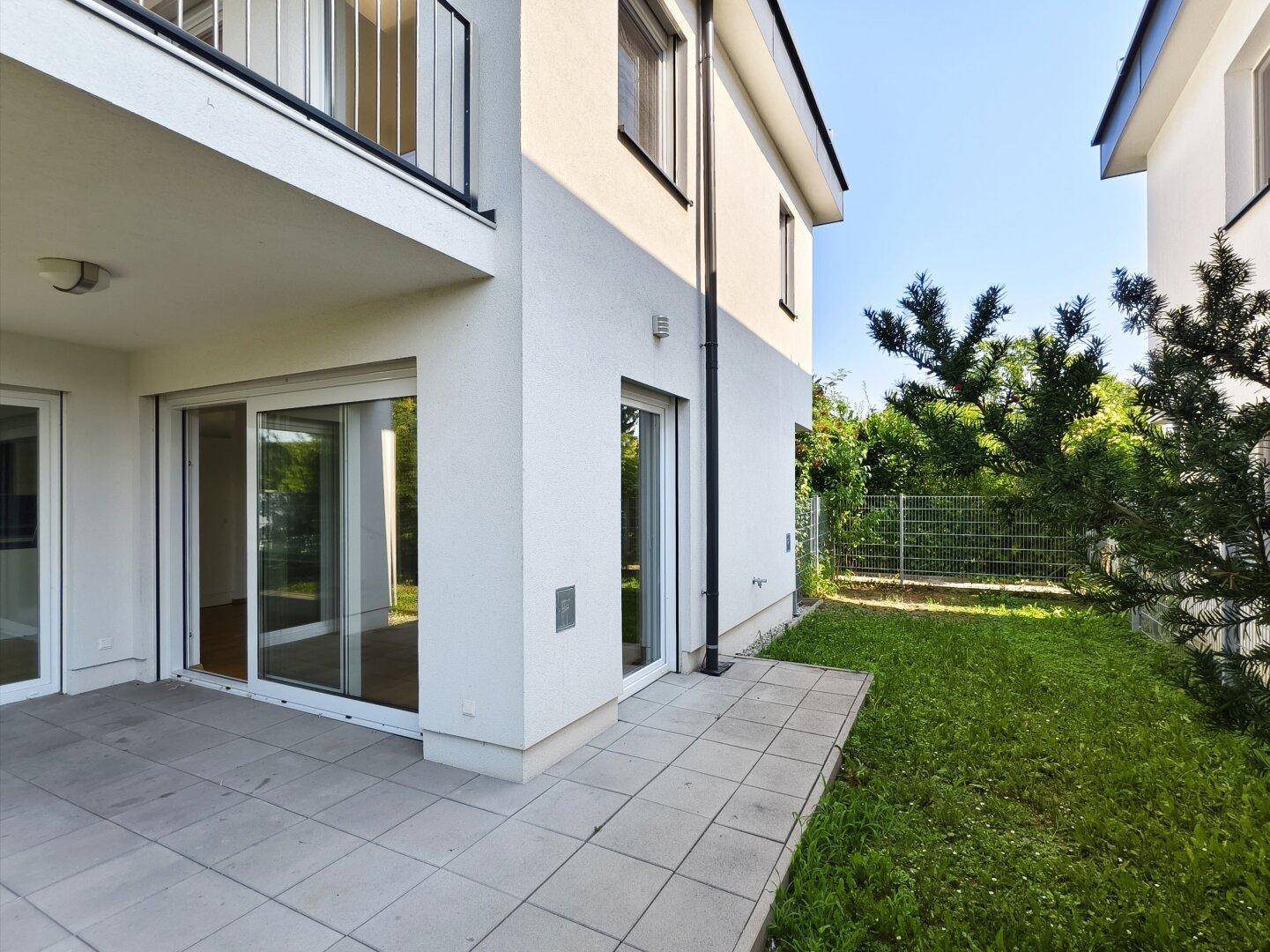 Seitliche Ansicht des Hauses mit gepflasterter Terrasse und grünem Rasen im Garten.