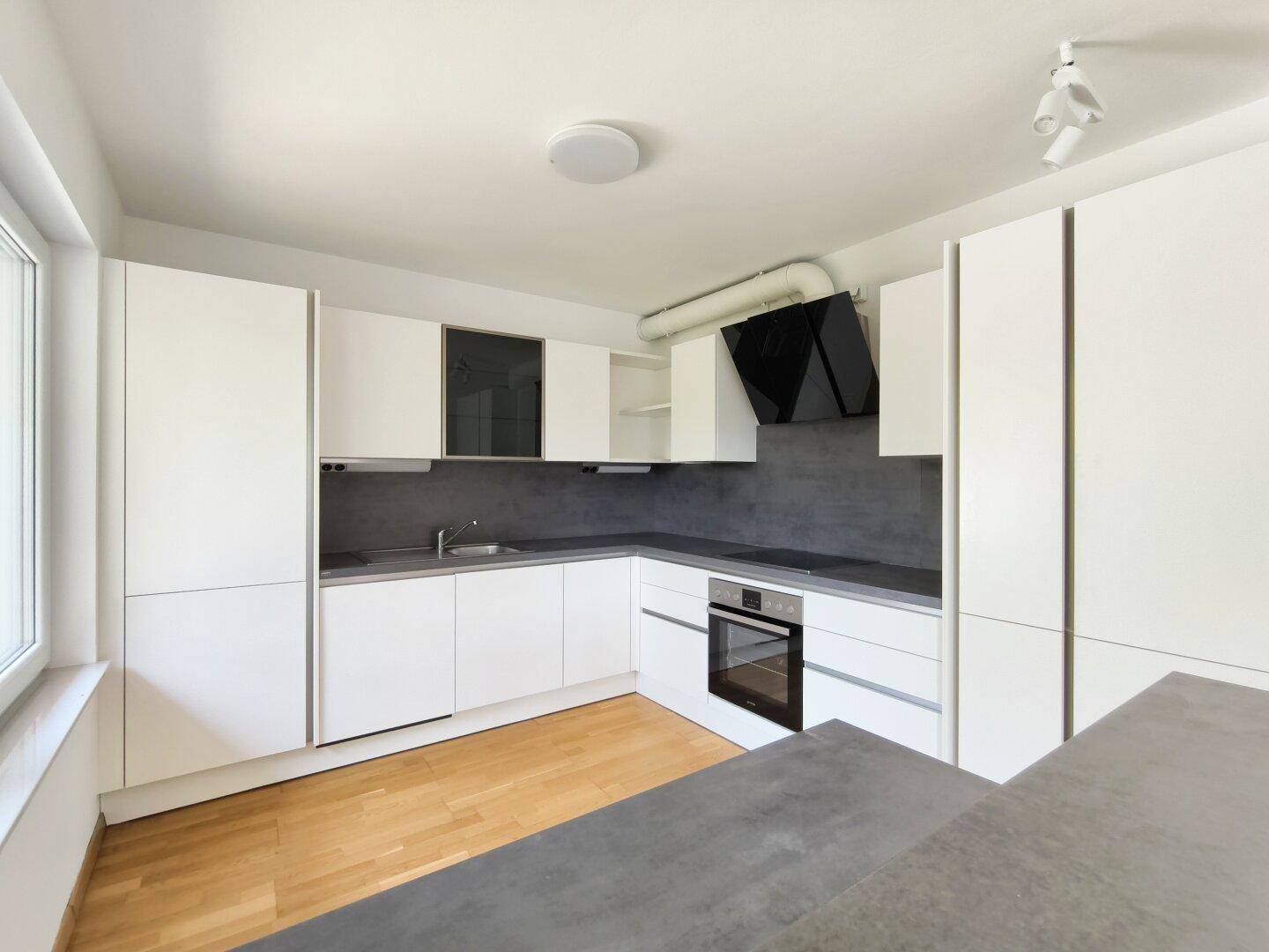 Voll ausgestattete moderne Küche mit weißen Fronten, Backofen und Dunstabzugshaube.