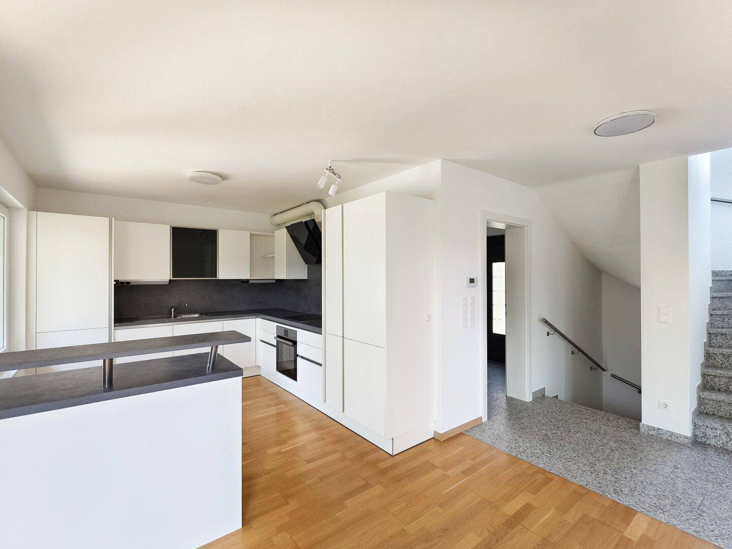 Moderne Einbauküche mit weiß-grauen Fronten und angrenzendem Treppenaufgang.
