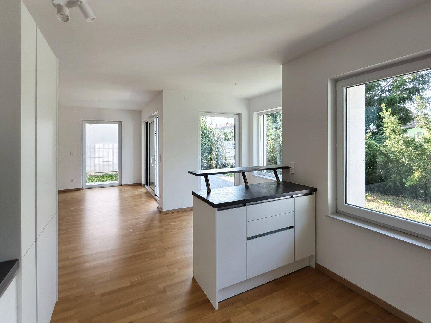 Offener Wohnbereich mit Holzboden, Bartheke und Blick auf den Garten durch große Fenster.