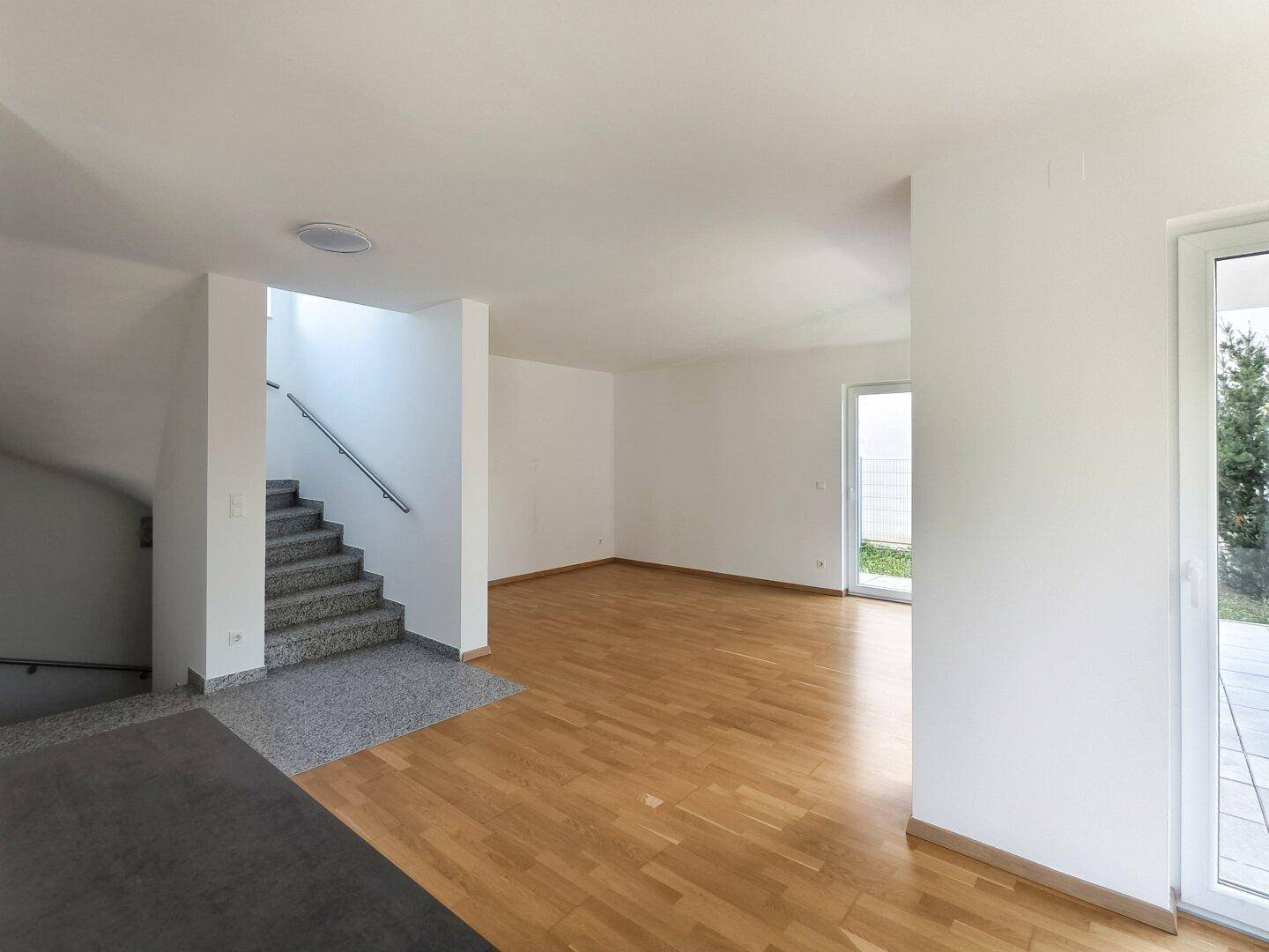 Geräumiger Wohnbereich mit Holzboden und offenem Treppenaufgang zum Obergeschoss.
