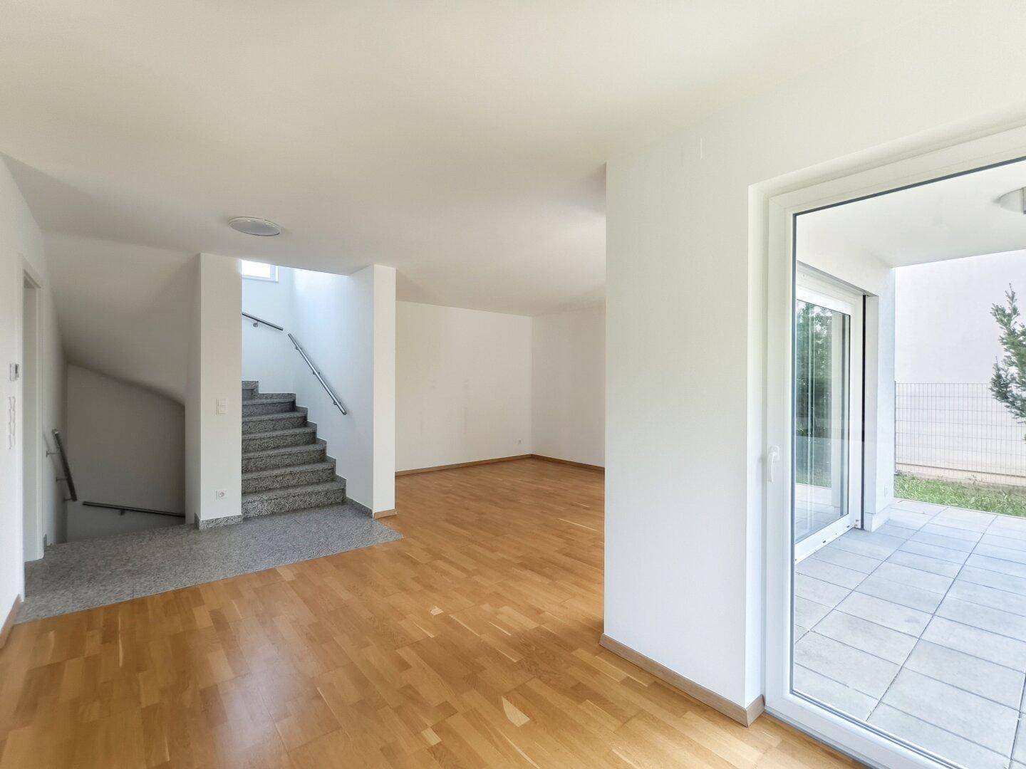 Heller Wohnbereich mit Zugang zur Terrasse und Treppe, die in die oberen Etagen führt.