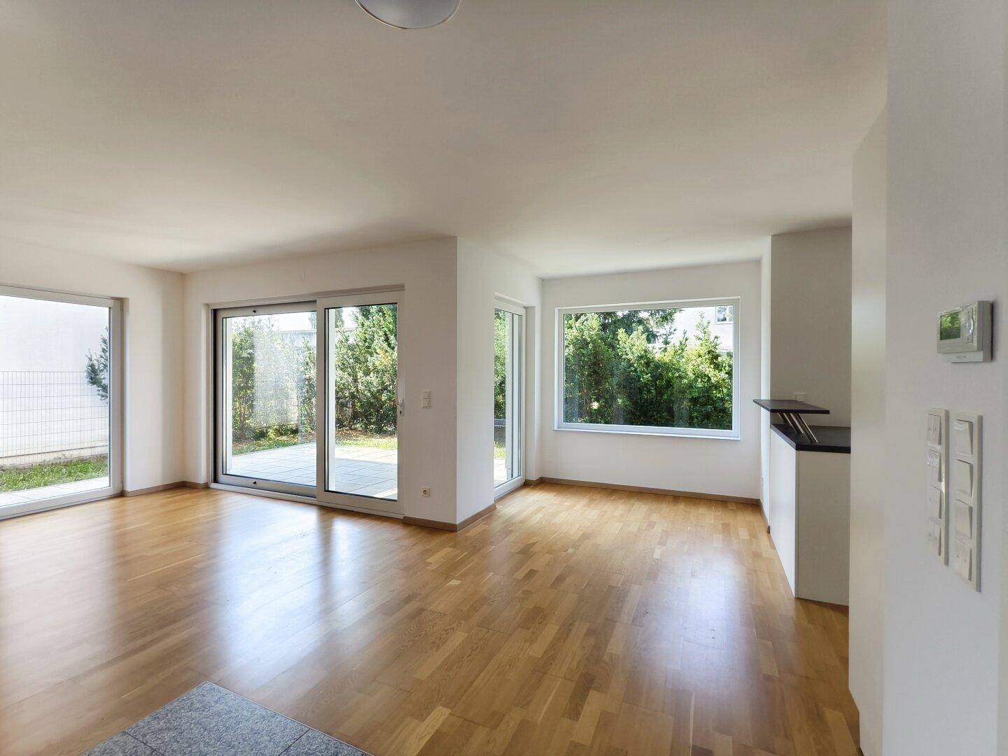 Lichtdurchfluteter Wohnbereich mit Holzboden und großen Fenstern, die viel Tageslicht hereinlassen.