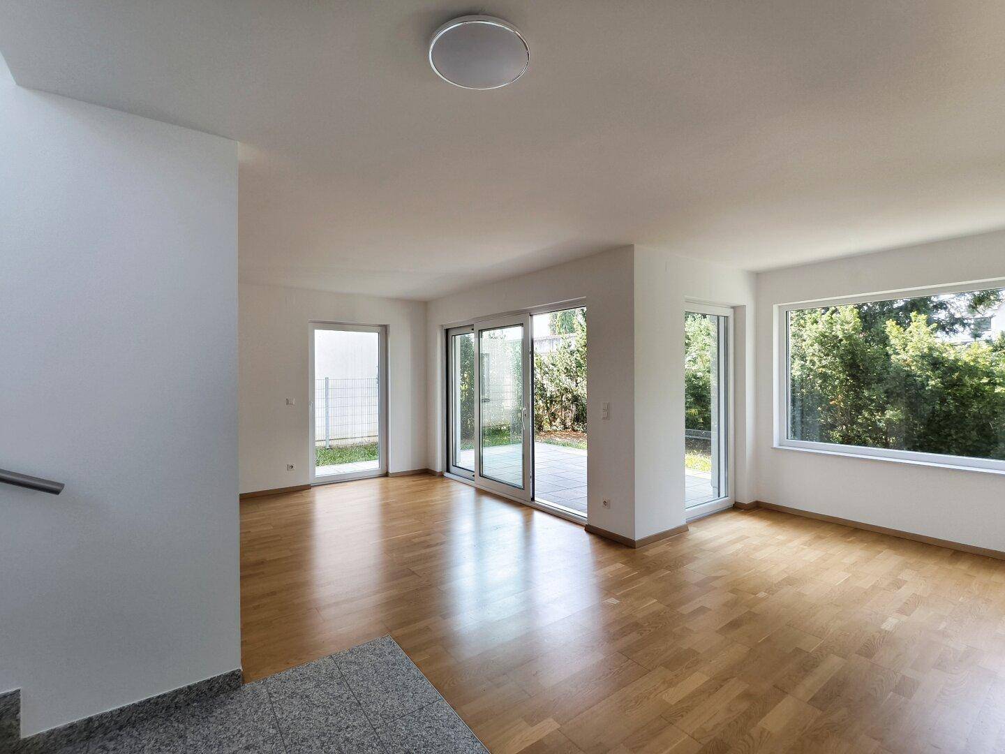 Geräumiger Wohnbereich mit Holzboden und Blick auf den Treppenaufgang sowie den Außenbereich.