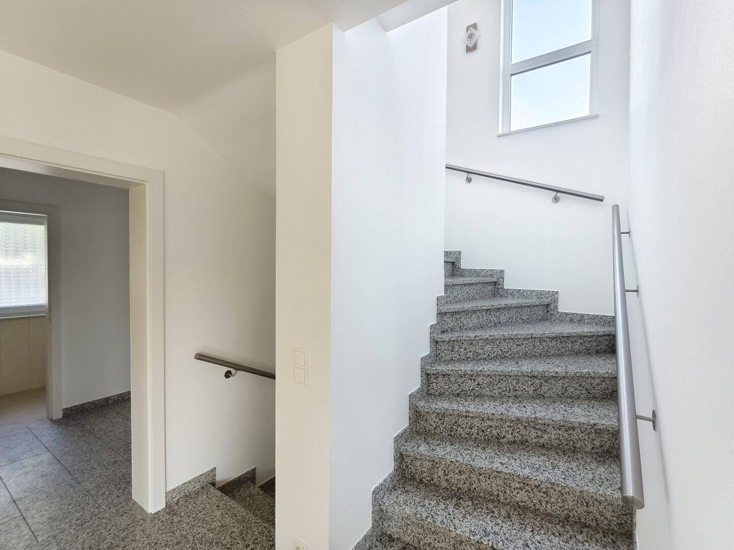 Treppenhaus mit Granitstufen und Edelstahlgeländer, das die Etagen verbindet.