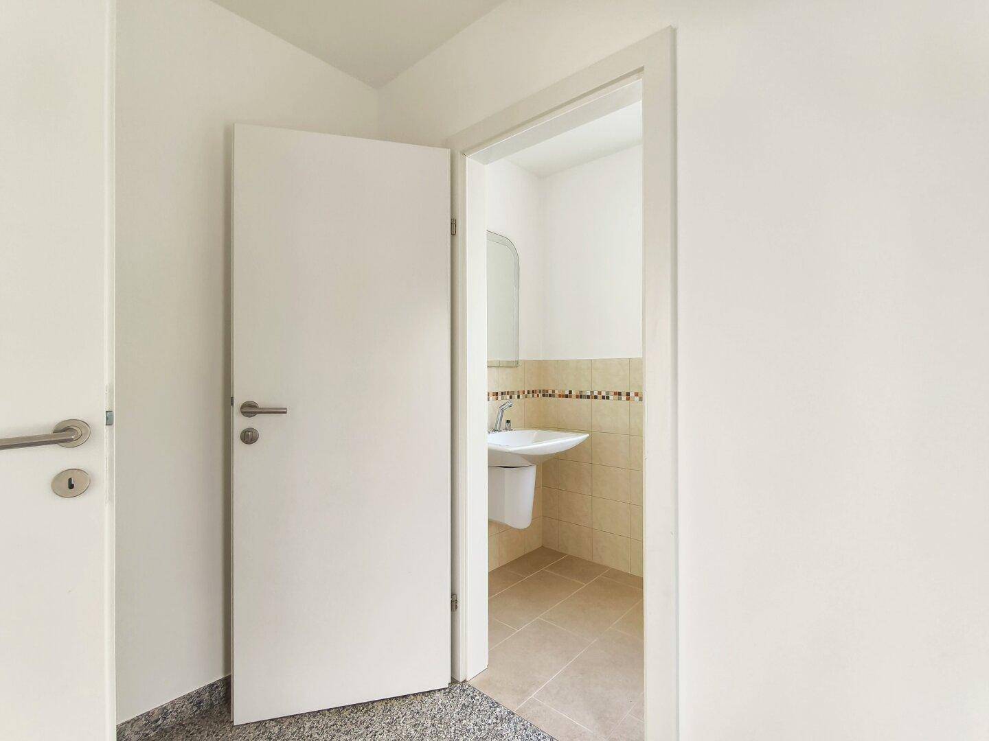 Kleines Gäste-WC mit Wandwaschbecken und hellen Fliesen an den Wänden.