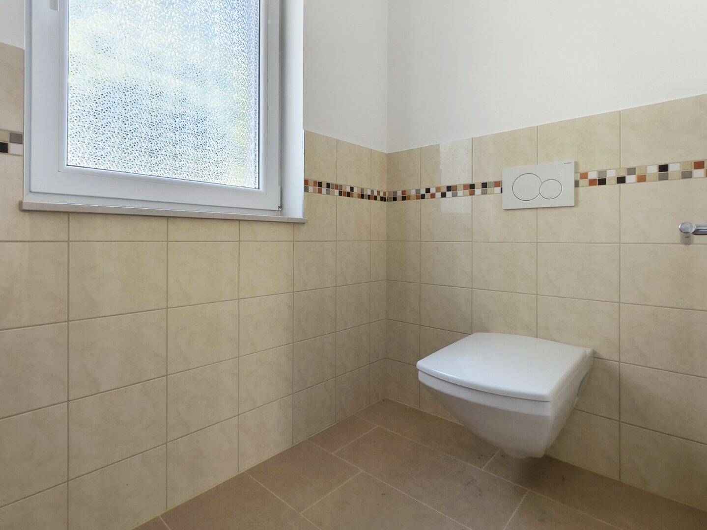Modernes Gäste-WC mit wandhängender Toilette, beigen Fliesen und Fenster für Tageslicht.