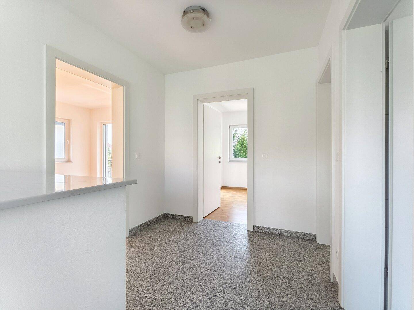 Heller Flur mit Granitboden und Durchgang zu weiteren Räumen im Erdgeschoss.