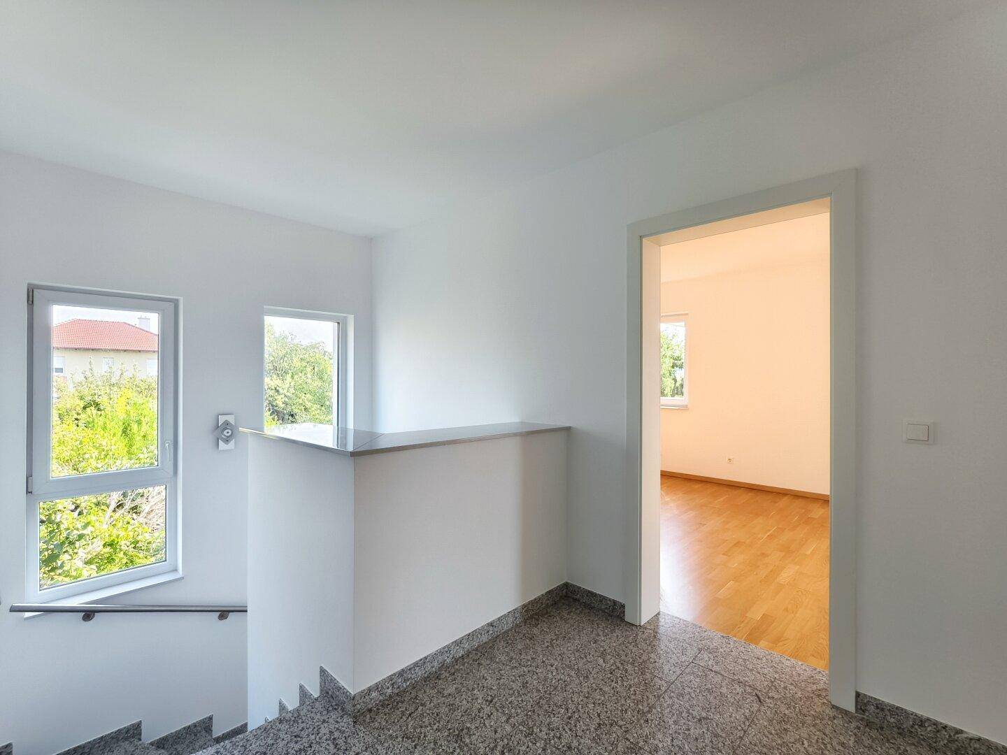 Heller Flur im Obergeschoss mit Granitboden und Blick auf den Treppenaufgang.